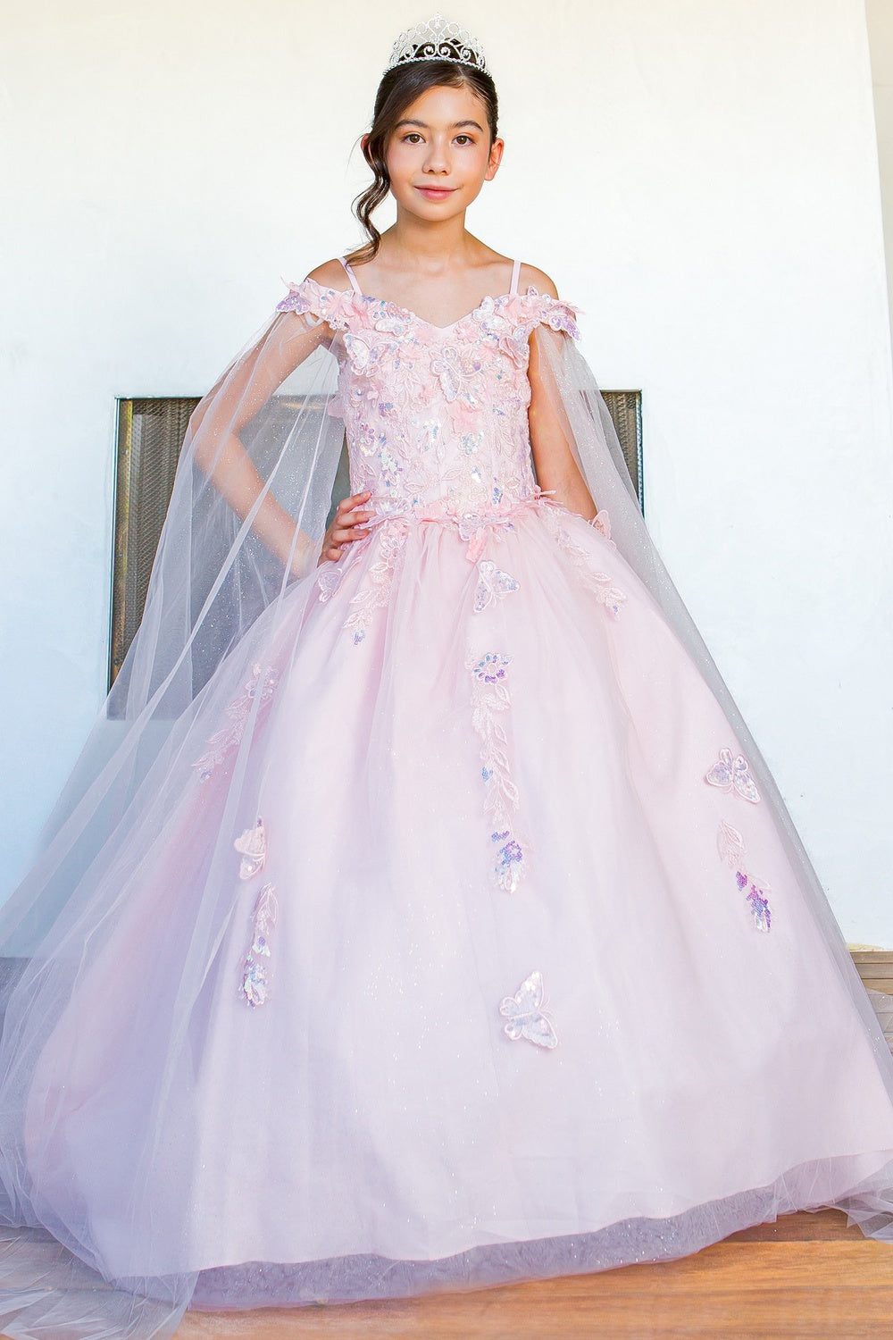 Young girl in a pink floral dress with a tiara indoors.Cinderella Couture 8075X 3D Floral Off-Shoulder Glitter Ball Gown